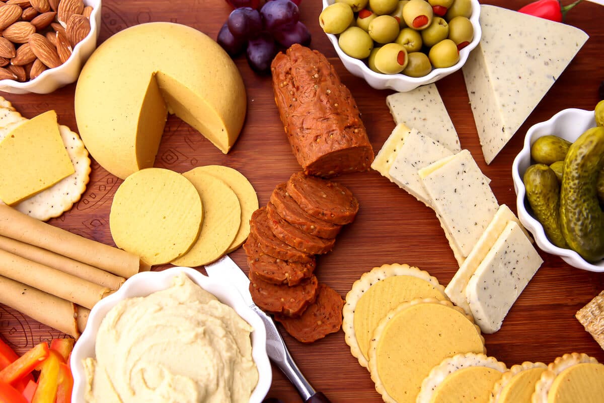 Una tabla de embutidos veganos con galletas, queso vegano, pepperoni vegano, pavo vegano, humus y aceitunas.