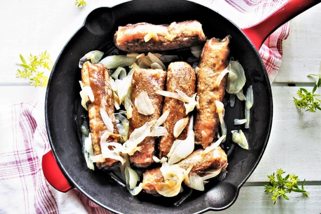 Salchichas de cerveza veganas con cebollas salteadas en una sartén de hierro.