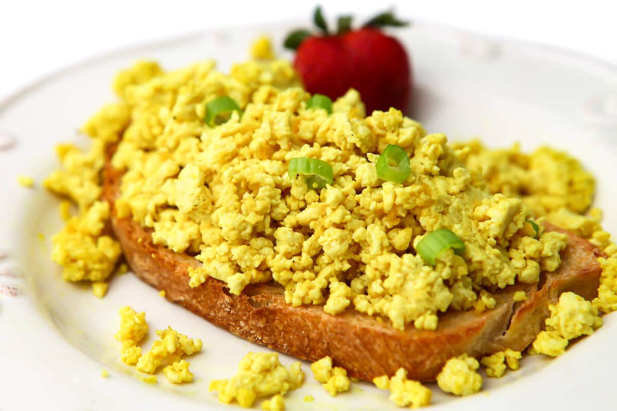 Huevos revueltos veganos sobre una tostada con una fresa al lado.