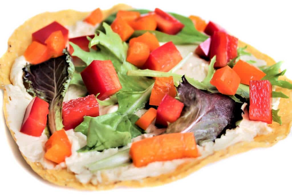 Una tostada vegana cubierta con hummus y pimientos picados y lechuga.