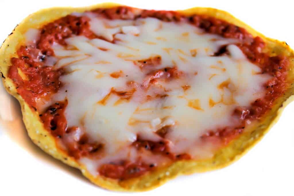 Una tostada vegana cubierta con salsa de pizza y queso vegano para hacer una pizza de tostada.
