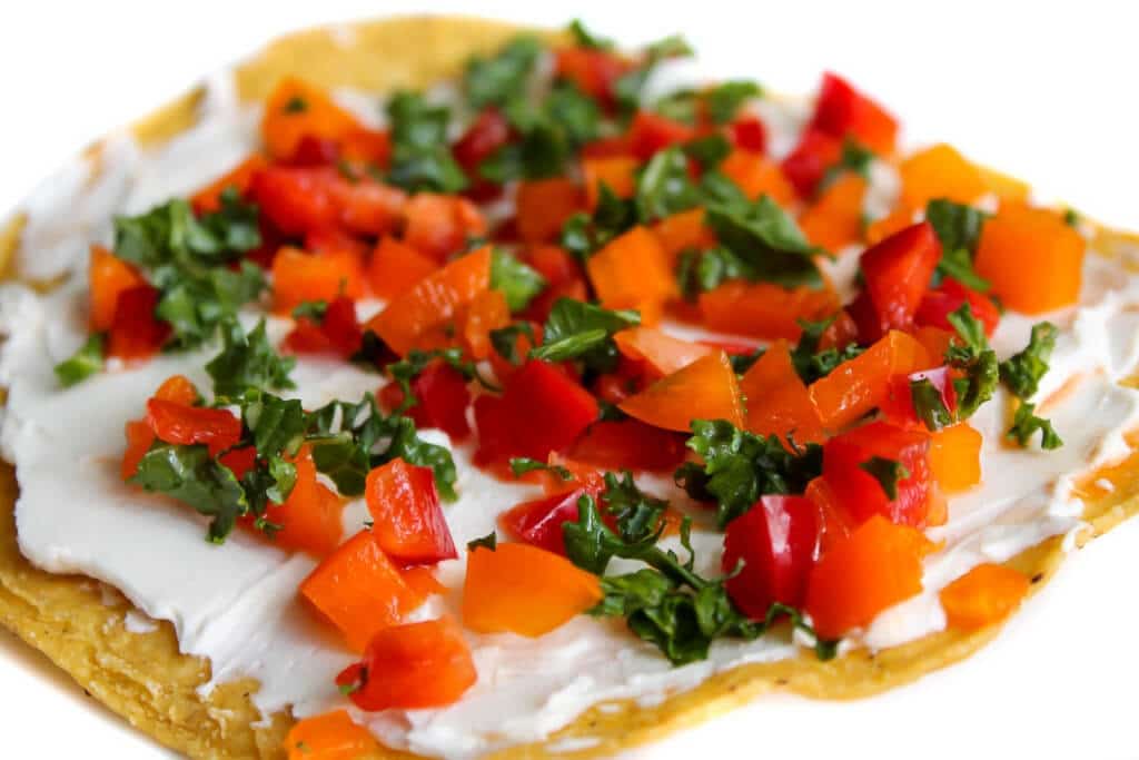 Una tostada vegana cubierta con crema de queso vegana y verduras picadas.