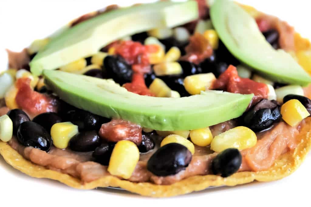Una tostada vegana sin gluten con frijoles refritos, frijoles negros, maÃz y aguacate.