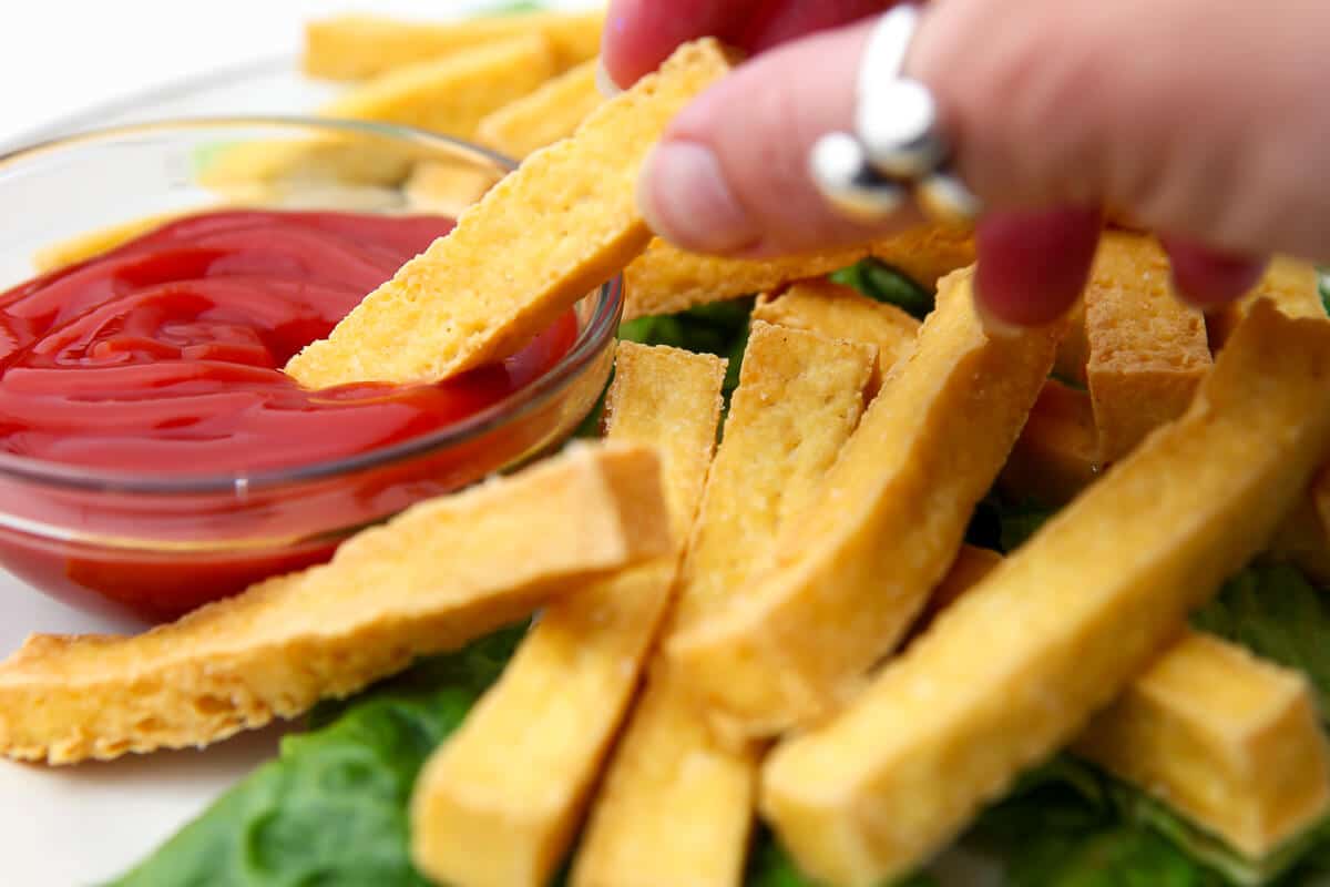 Una mano mojando una fritura de tofu en ketchup.